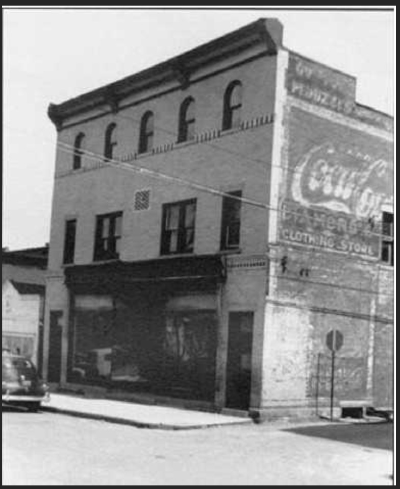 Brick commercial building with five arched upper windows and painted Coca-Cola advertising on its side wall