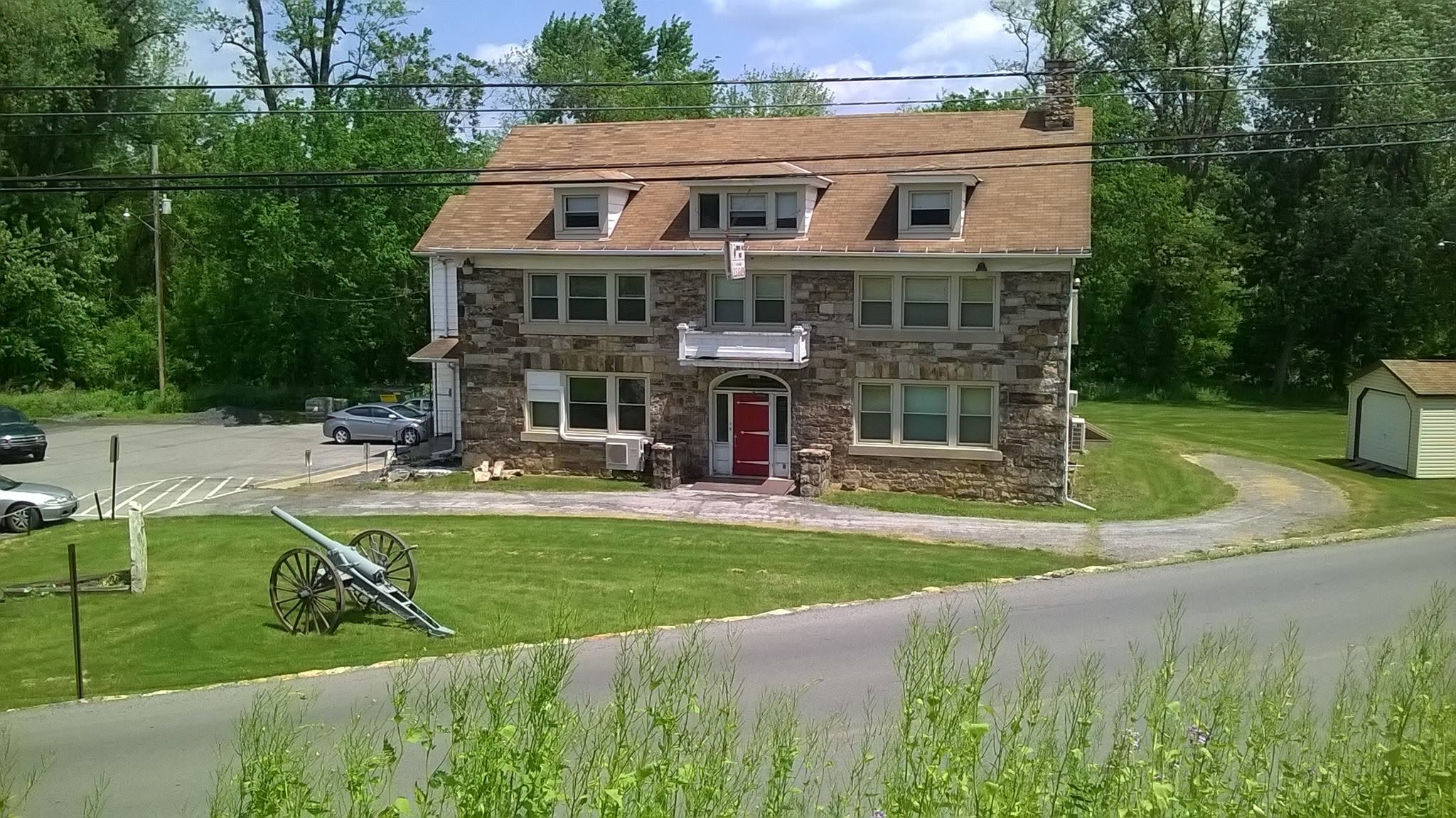 Front view of the Stone House during its American Legion era, with the stone facade, red entrance door and memorial cannon visible